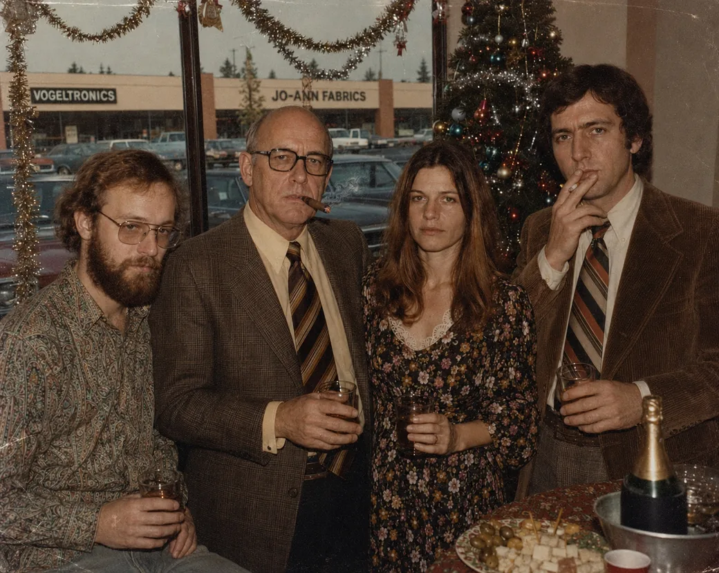 Four people at a company Christmas party in the banquet room at Rosarita's, late 1970s &mdash; Ray Kessler, Walter T. Vogel with a cigar, Diane Vogel, and Walter T. Vogel Jr. &mdash; with a decorated tree behind them and the VogelTronics building visible through the window